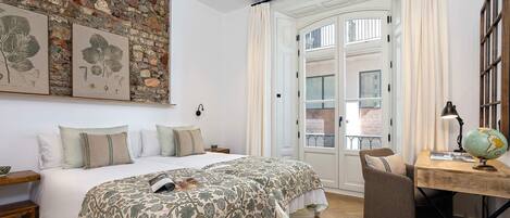A bedroom with two beds, a desk with a globe, and a brick wall with botanical prints.