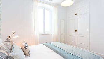 Un dormitorio con cama, lámpara de noche, ventana con cortinas y armario.