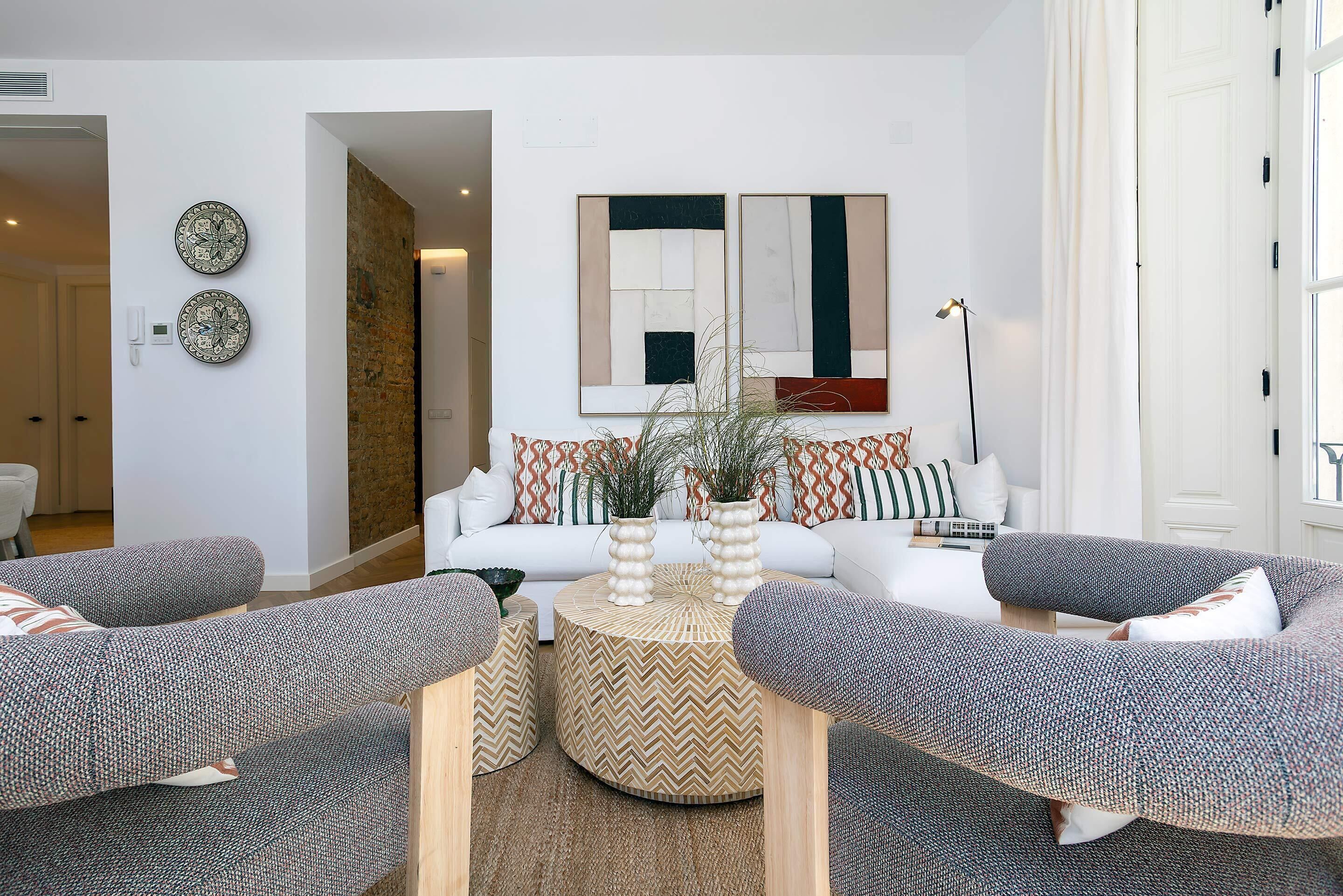 Ein modernes Wohnzimmer mit einer Sofagarnitur, einem Couchtisch, dekorativen Vasen und einer Wand mit abstrakter Kunst.
