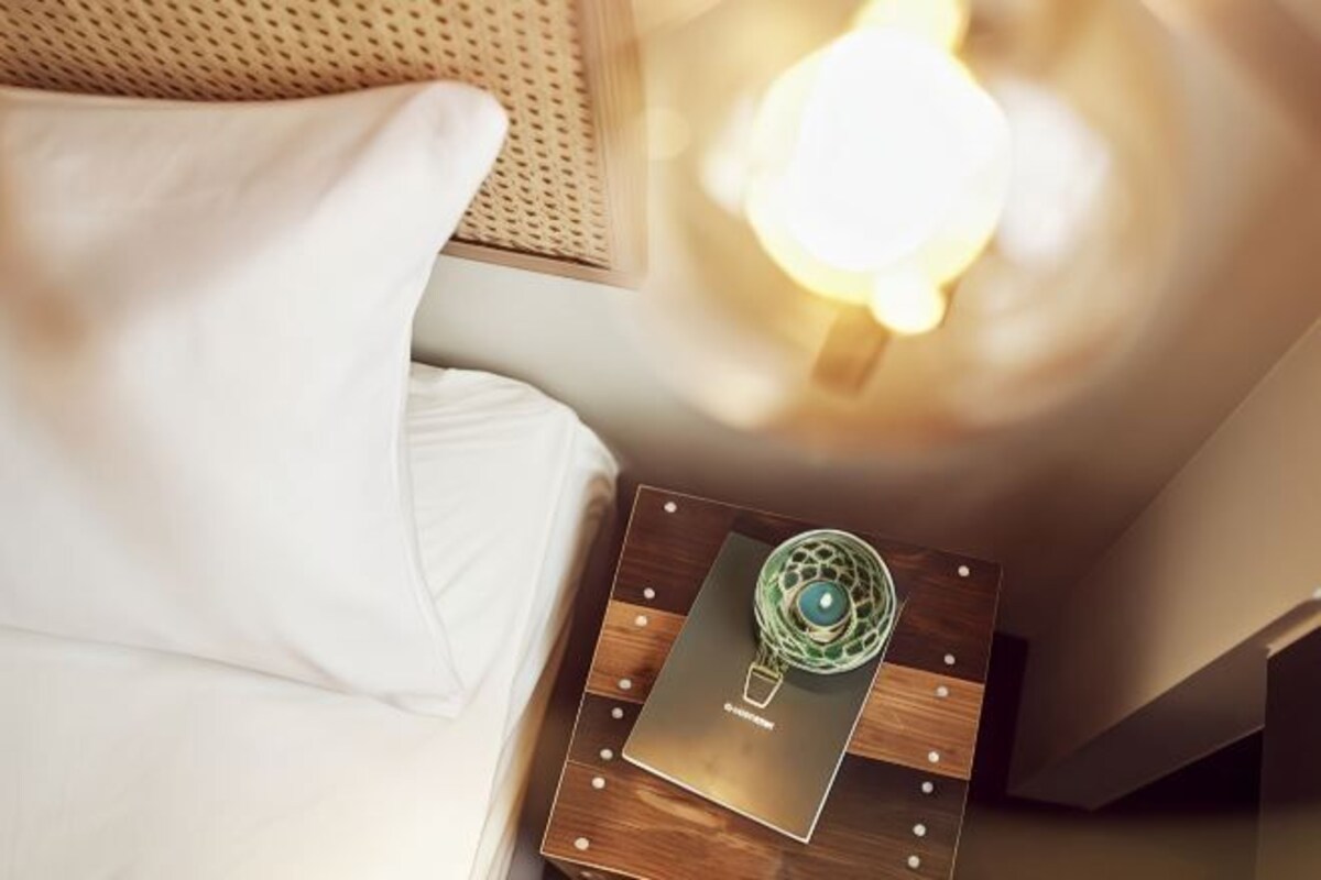 A neatly made bed with a white pillow and a wooden bedside table with a decorative item on it.