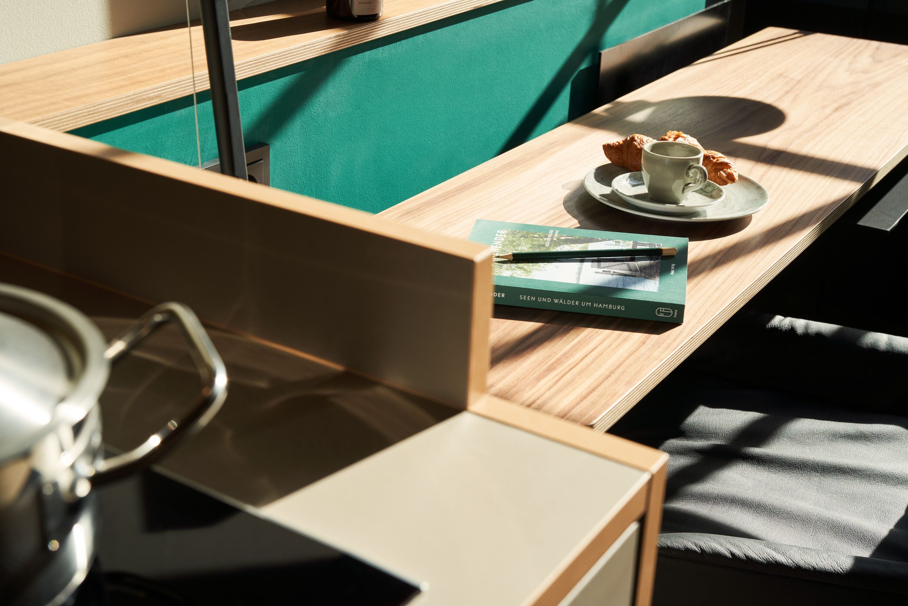 A neatly arranged workspace with a laptop, a cup of coffee, croissants, and a book on a wooden table.