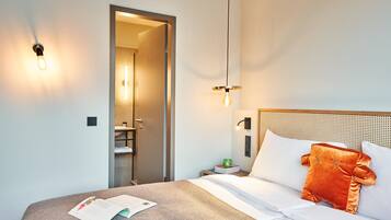 Une chambre d’hôtel comprenant un lit, une table de chevet, une lampe de lecture et une porte donnant accès à une salle de bain.