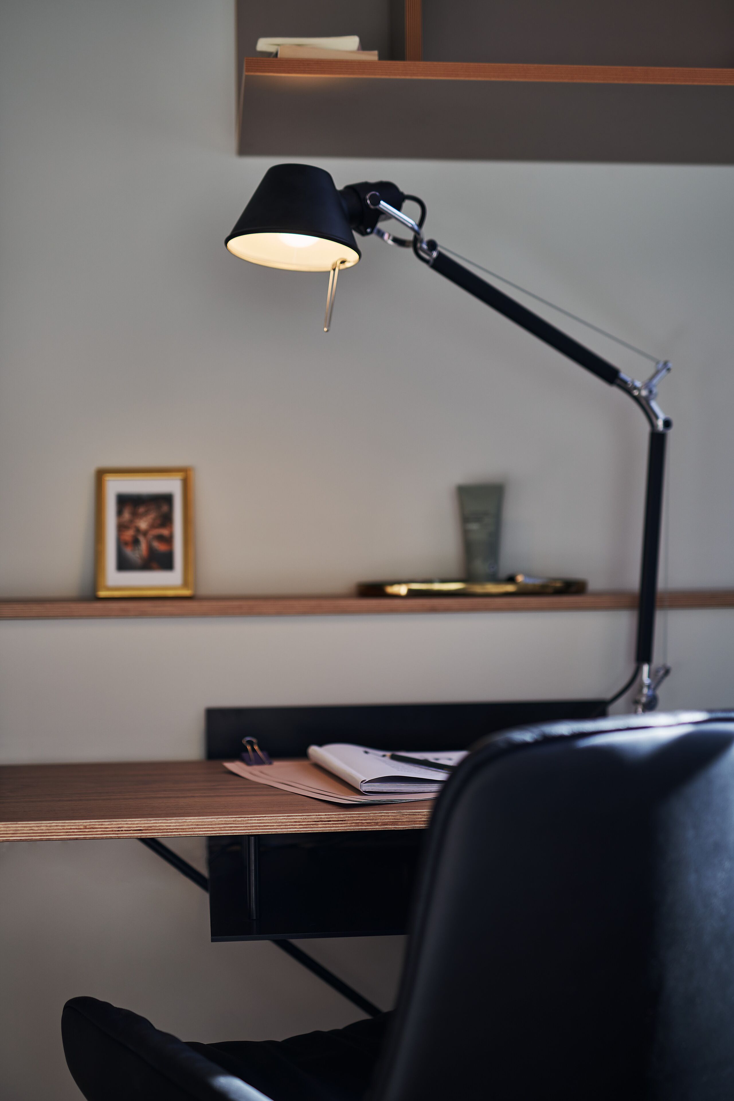 Een bureau met een lamp, een lijst met een foto en een plank met boeken.