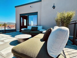 Ein zeitgemäßer Außenbereich zum Sitzen mit einer Couch, Sesseln, einem runden Tisch und einem Blumentopf.