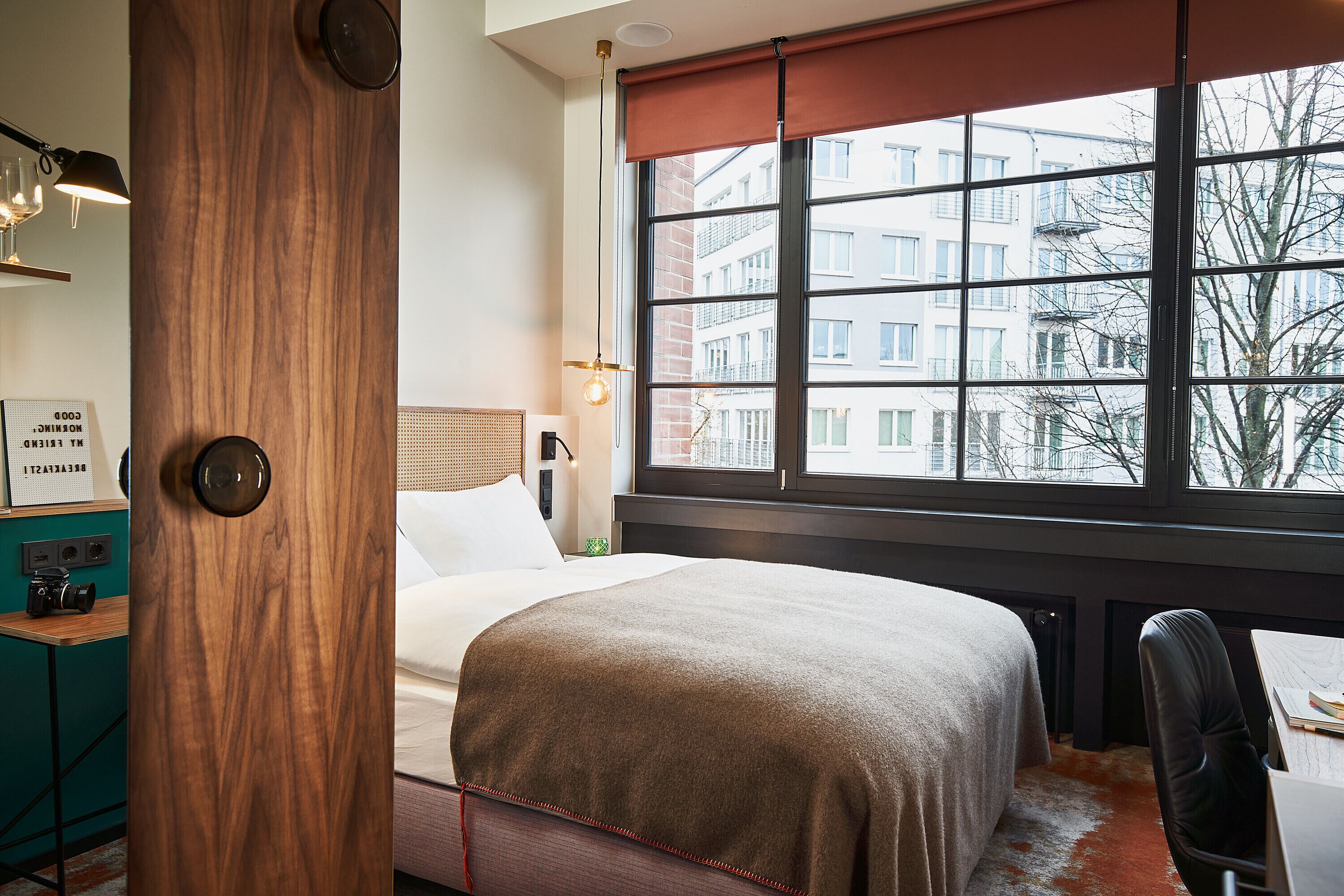 A hotel room with a large window, a bed, a desk, and a chair.
