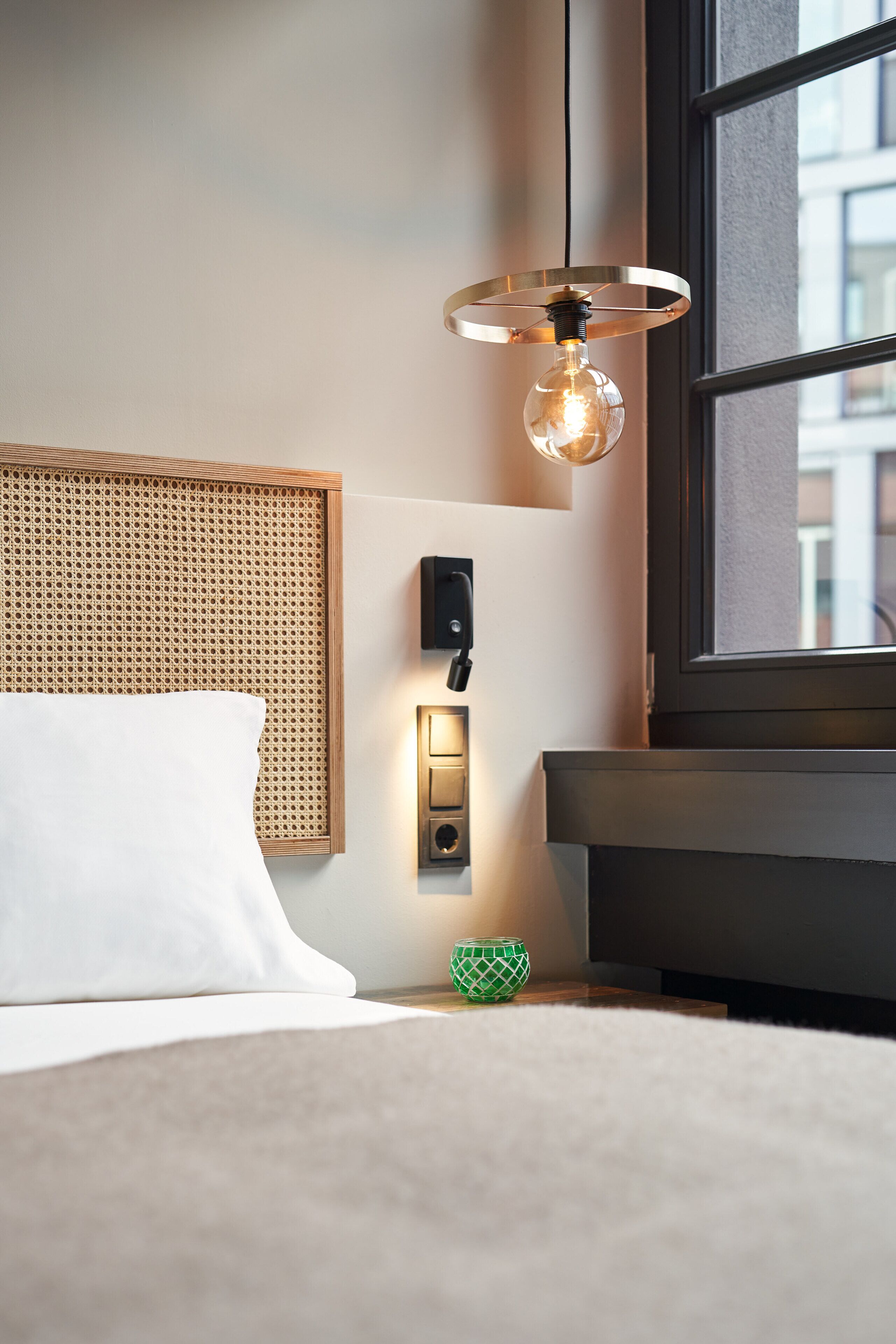 A hotel room with a bed, a wall-mounted light fixture, a thermostat, and a window.