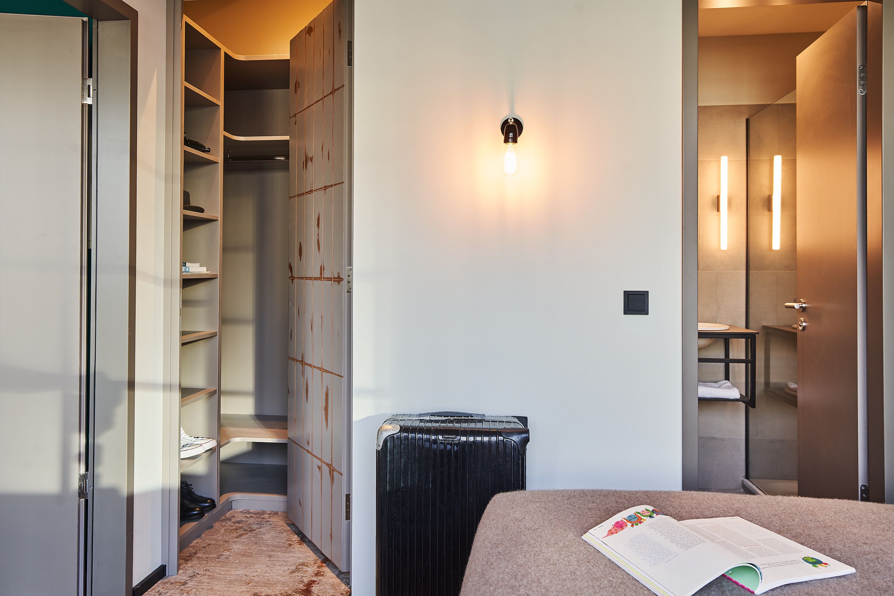 Habitación de hotel con cama, radiador, armario y baño visible a través de una puerta abierta.