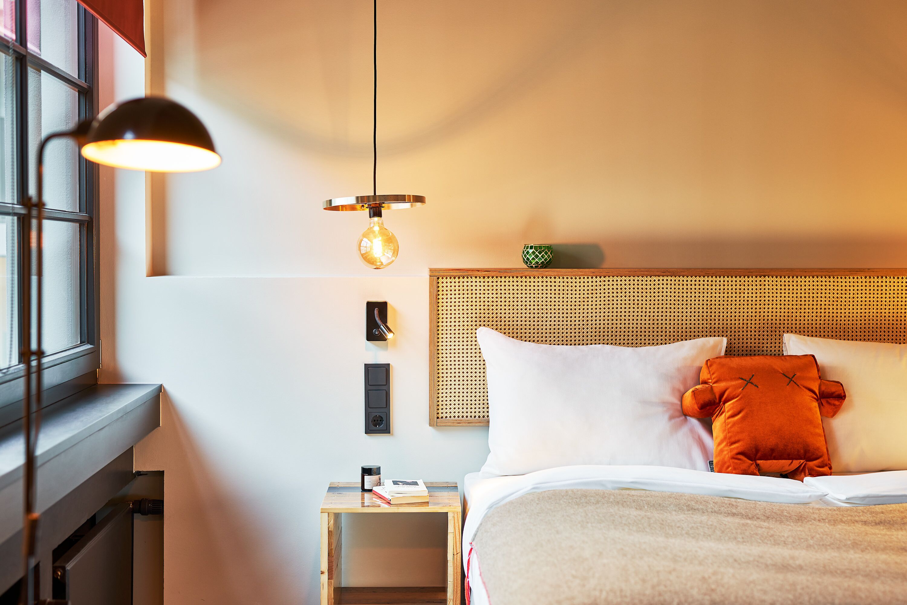A neatly arranged hotel room with a bed, a bedside table, a lamp, and a wall-mounted light fixture.