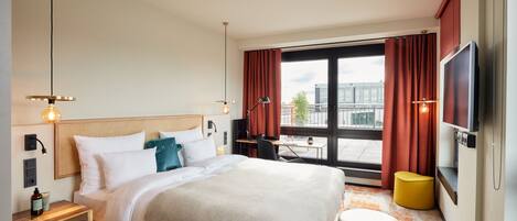 A modern hotel room with a large bed, a desk, a TV, and a window with curtains.