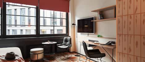 A modern room with a large window, a desk, a chair, a sofa, and a TV.