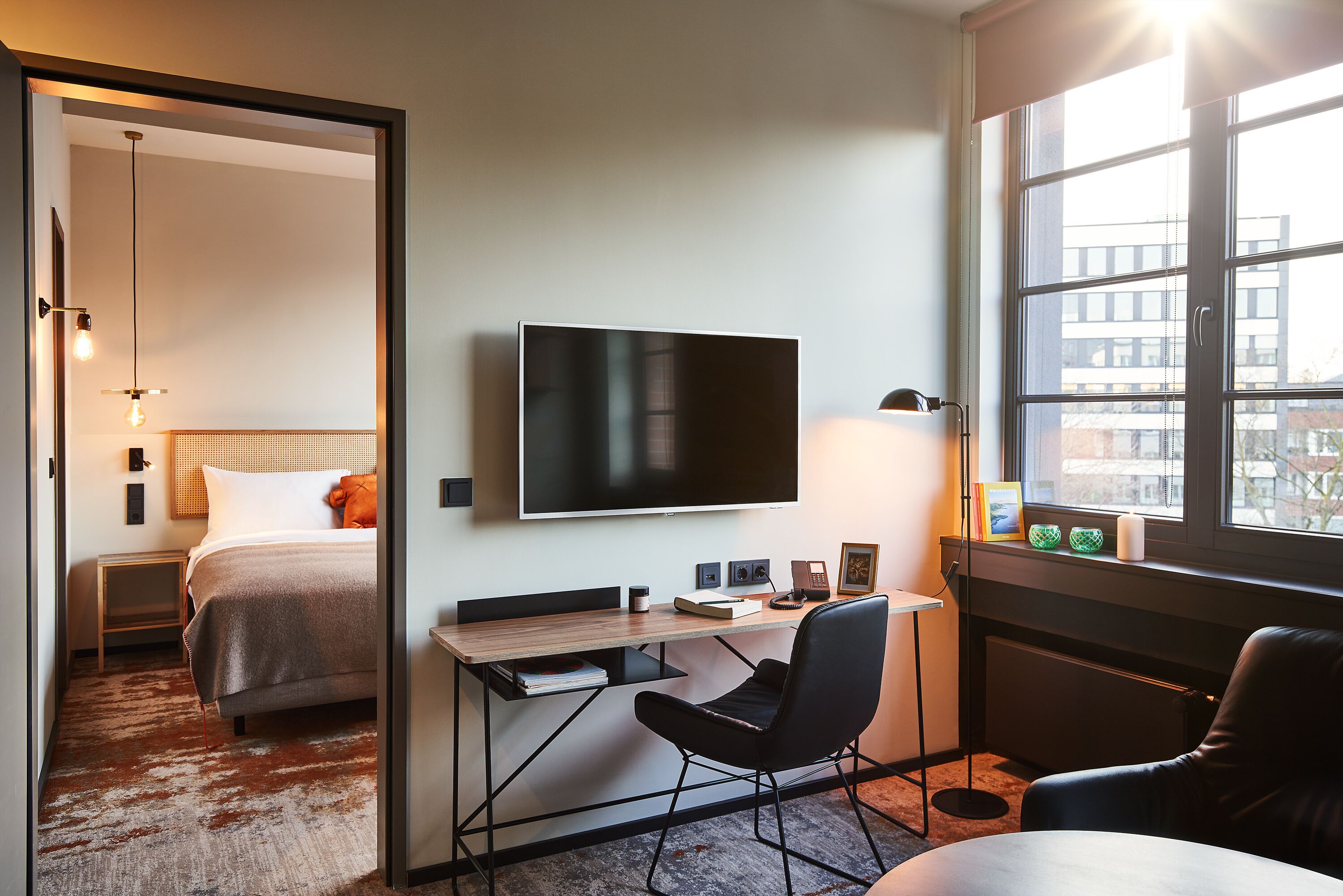Habitación de hotel con cama, escritorio con silla, televisor y ventana con vistas a edificios.