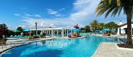 A swimming pool with lounge chairs and umbrellas, surrounded by palm trees and a clear sky.