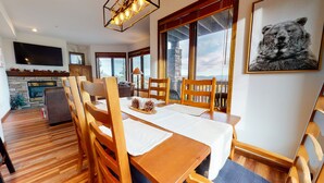 Un coin repas avec des chaises et une table en bois, une cheminée et une grande fenêtre donnant sur un beau paysage.