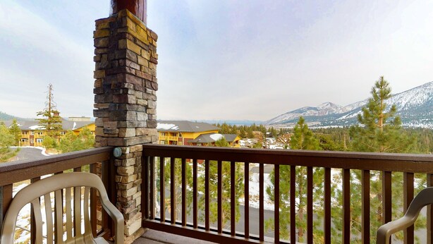 Un balcon orné d’un pilier en pierre, donnant sur un quartier résidentiel avec des maisons et une chaîne de montagnes.