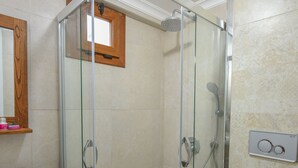Casa de banho com cabine de duche em vidro, toucador de madeira, lavatório branco e sanita.