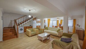 Uma sala de estar espaçosa, com escadas, sofás, uma mesa de centro e cozinha ao fundo.