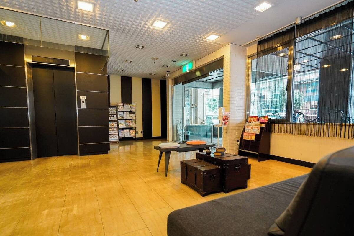 A modern lobby with a wooden floor, a reception desk, a seating area with a sofa, and a bookshelf.