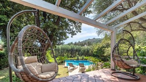 Eine Terrasse mit zwei Korbstühlen, einem Pool und Blick auf einen üppigen Garten.