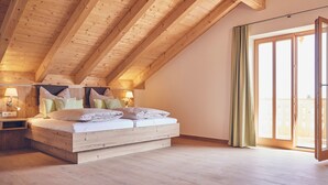 Ein Schlafzimmer mit geneigter Decke, einem großen Bett mit vielen Kissen, Nachttischlampen und einer Glastür, die zu einem Außenbereich führt.