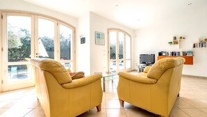 Un salón amplio con dos sillones amarillos, una mesa de centro de cristal, un televisor de pantalla plana y una estantería.