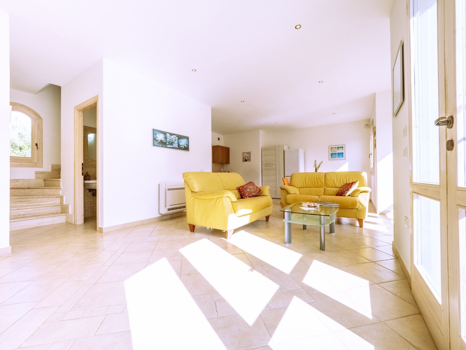 A spacious living room with two yellow sofas, a glass coffee table, and a staircase leading to another level.
