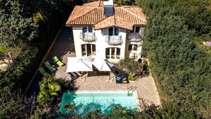 Una casa de dos pisos con techo de tejas, piscina y un patio con mobiliario exterior.