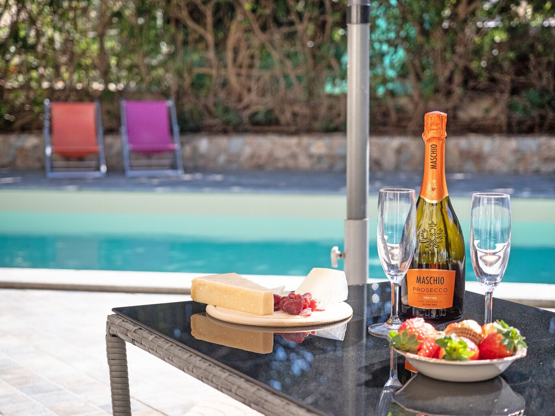 A table with a bottle of Maschio Prosecco, two glasses, a plate of cheese and strawberries, and a bowl of fruit.
