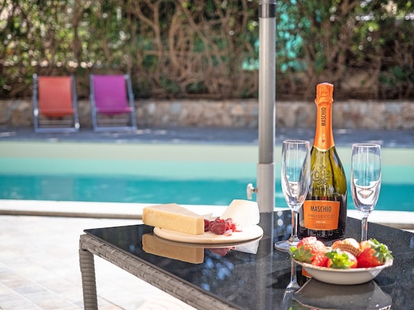 A table with a bottle of Maschio Prosecco, two glasses, a plate of cheese and strawberries, and a bowl of fruit.