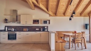 Een moderne keuken met houten balken, een eethoek met een tafel en stoelen, en inbouwapparatuur.