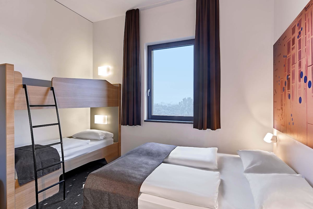 A hotel room with a bunk bed, a single bed, and a window with curtains.