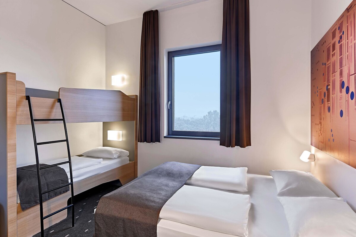 Une chambre d’hôtel avec un lit superposé, un lit simple et une fenêtre avec des rideaux.