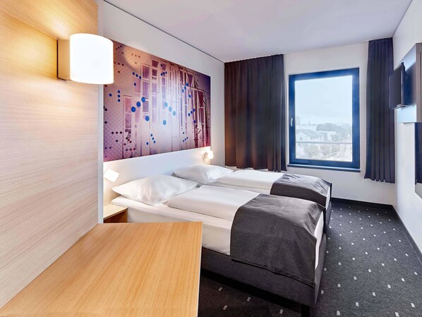 Habitación de hotel con dos camas, un ventanal grande y una pared con diseño geométrico.