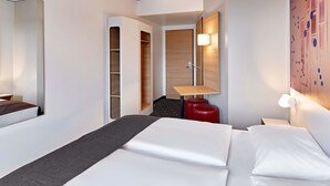 Een moderne hotelkamer met een bed, een bureau, een kledingkast en een wandlamp.