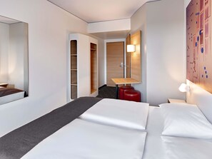 Une chambre d’hôtel moderne équipée d’un lit, d’un bureau, d’une armoire et d’une lampe fixée au mur.