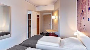 Een hotelkamer met een bed, een kledingkast, een bureau en een wandlamp.
