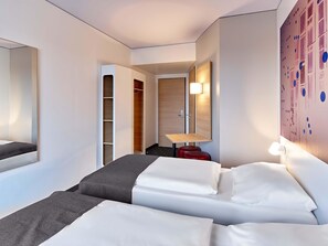 Une chambre d’hôtel équipée d’un lit, d’une armoire, d’un bureau et d’une lampe fixée au mur.