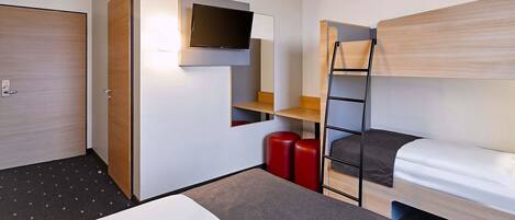 Una habitación de hotel moderna con una cama litera, un escritorio con silla, un televisor de pantalla plana montado en la pared y una pequeña zona de estar con taburetes.