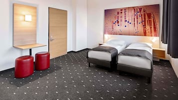 Een hotelkamer met een bed, twee rode krukken, een houten deur, een wandlamp en een schilderij.