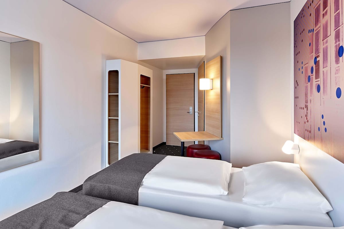 A hotel room with a bed, a wardrobe, a desk, and a wall-mounted lamp.