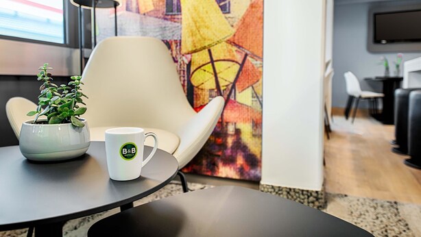 Una habitación de hotel moderna con una mesa redonda, una planta en maceta, una taza, un sillón cómodo y un mural colorido en la pared.