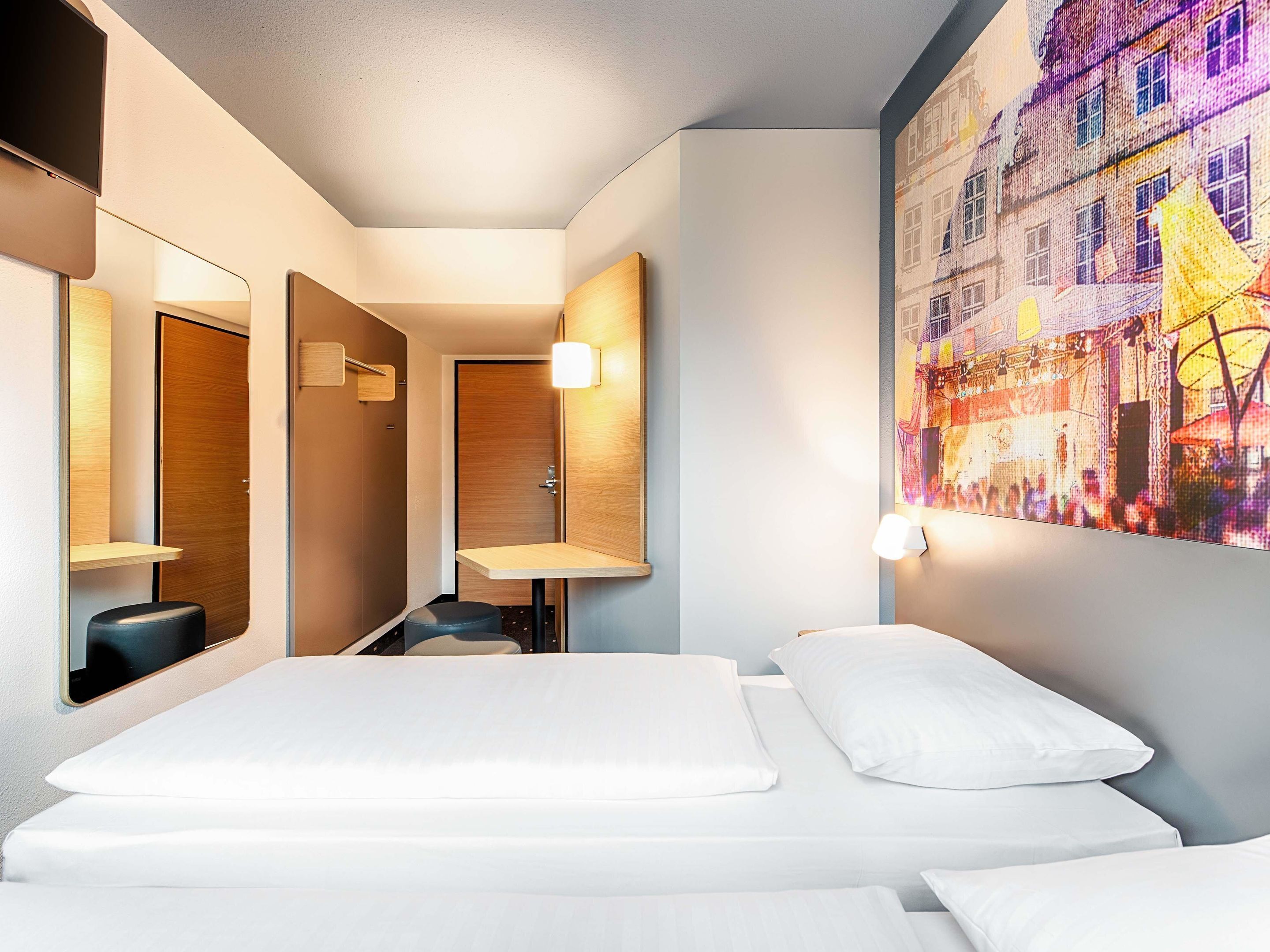 A hotel room with a bed, a mirror, a small desk, and a wall-mounted TV.