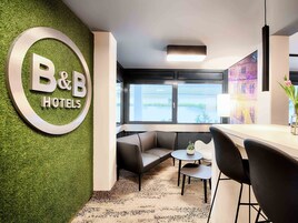 Un hotel B&B con vestíbulo, una pared verde, una recepción, un área de estar con sofá y sillones, y un ventanal con vistas.