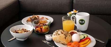 A breakfast setting with a bowl of cereal, a glass of orange juice, a plate with eggs, vegetables, and a muffin on a round table.