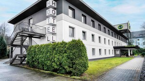 A modern hotel building with a staircase leading to the entrance, a reception area, and a well-maintained lawn. - B&B Hotel Bielefeld-Ost (Bielefeld)