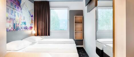 Habitación de hotel con dos camas, un escritorio, una silla, un estante y un ventanal con vista a árboles.
