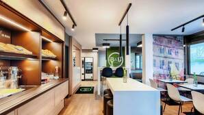A modern hotel lobby with a reception desk, seating area, and a buffet counter. - B&B Hotel Bielefeld-Ost (Bielefeld)