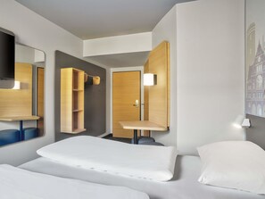 Ein modernes Hotelzimmer mit Bett, Schreibtisch, Spiegel und einer Wandablage.
