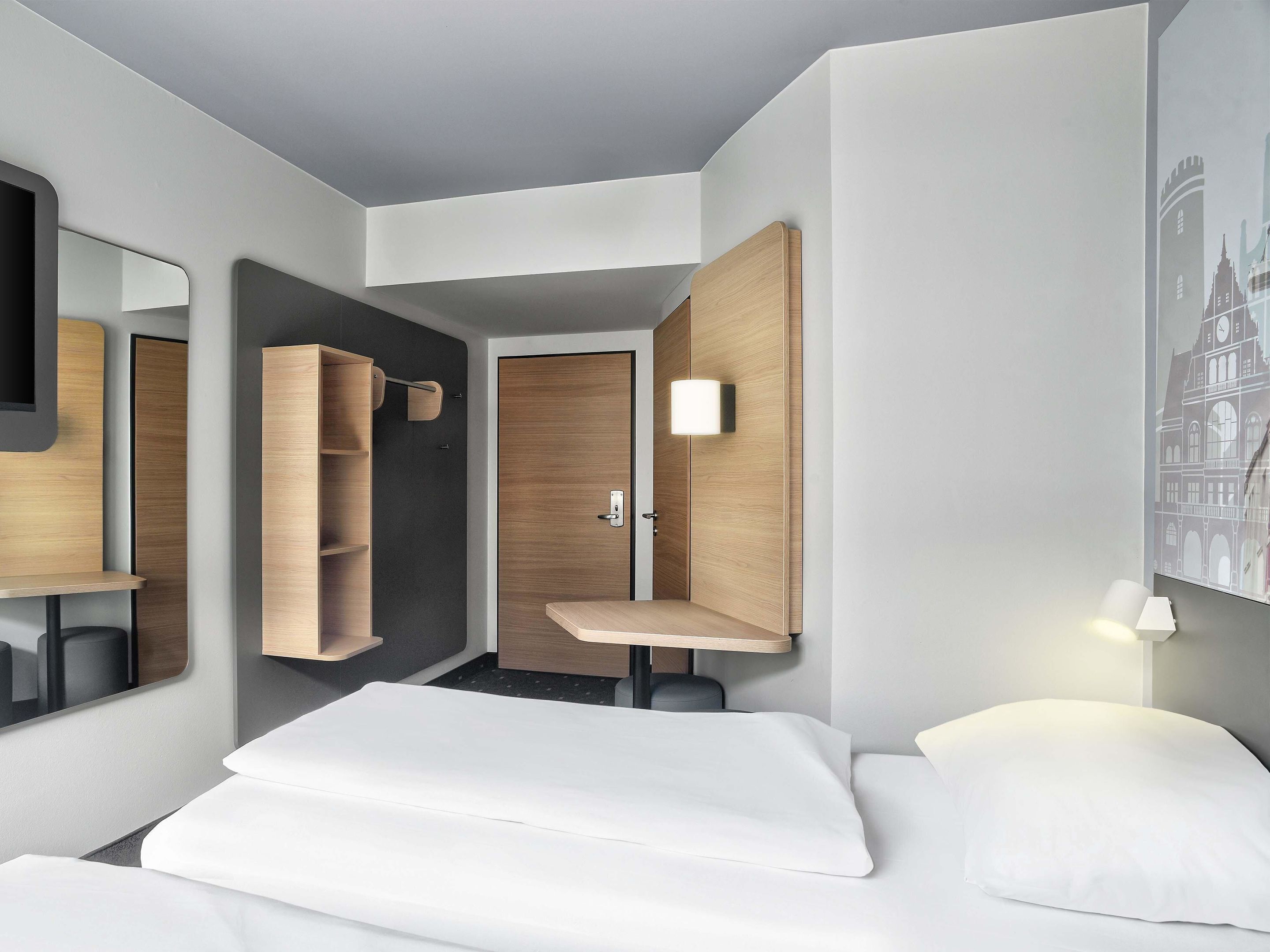 Ein modernes Hotelzimmer mit einem Bett, einem Schrank, einem Spiegel und einer Wandleuchte.