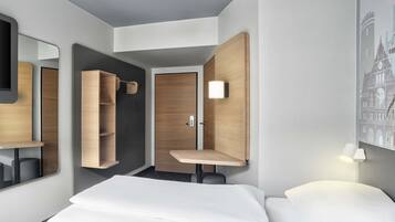 Ein modernes Hotelzimmer mit einem Bett, einem Schrank, einem Spiegel und einer Wandleuchte.