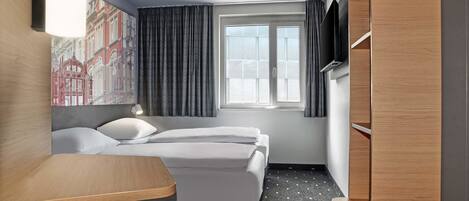 Una habitación de hotel con cama, escritorio, silla, armario y ventana con cortinas.